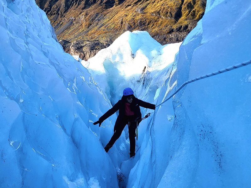 A roped climber bracing against the blue walls of a deep crevasse