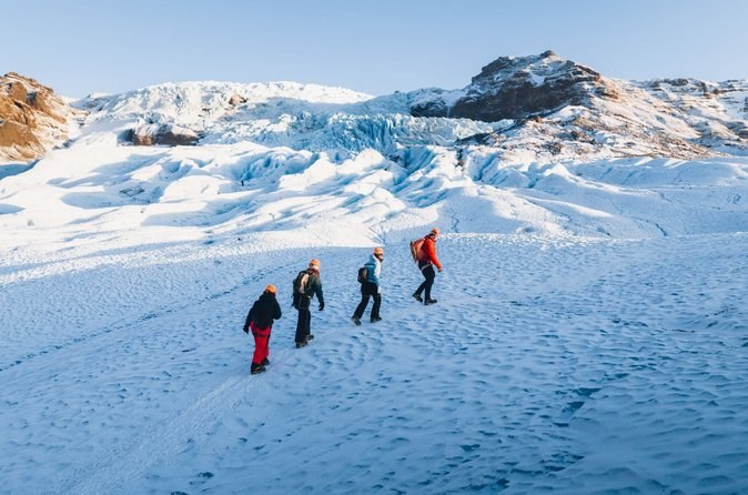 Four hikers climbing a snow-covered glacier slope toward a crevassed icefall