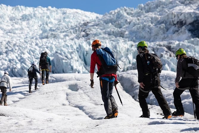 Hikers in helmets and crampons, seen from behind, walking toward a broken icefall