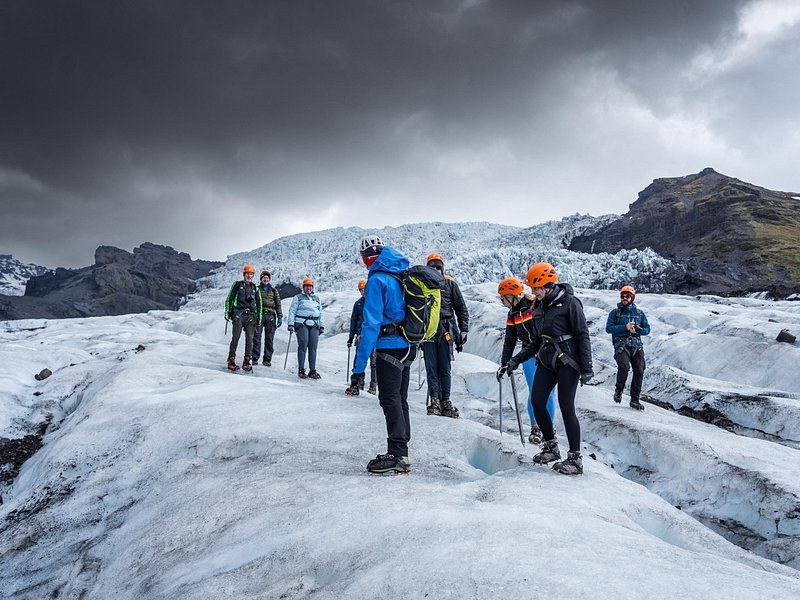 A guided group in helmets on grey glacier ice under a dark storm sky