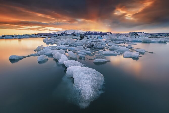 Icebergs drifting on a still glacier lagoon under an orange sunset sky