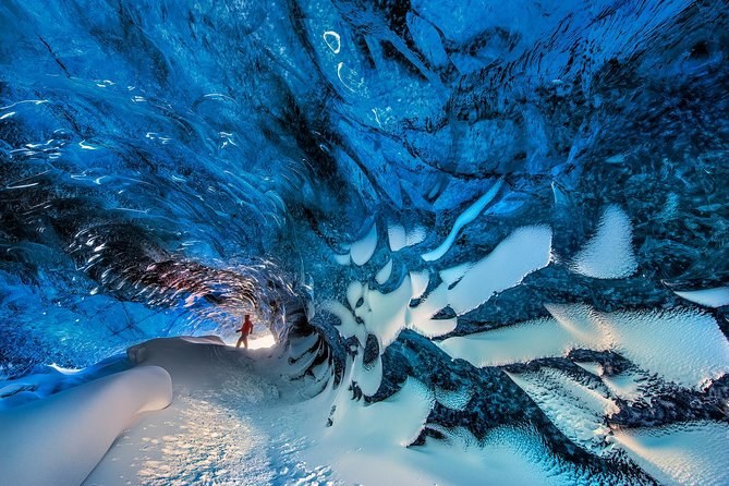 Daylight glowing through the blue roof of an ice cave, a visitor small inside