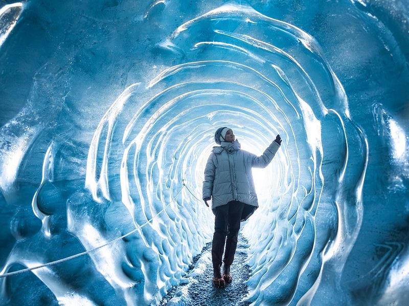 A visitor seen from behind reaching up inside a ringed blue ice tunnel