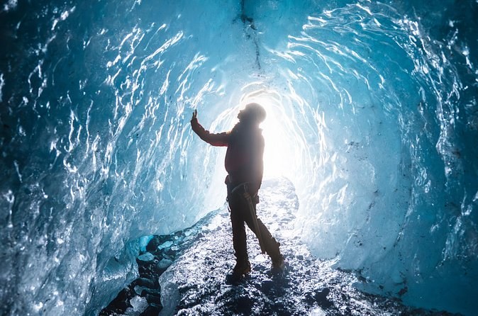 A visitor in silhouette at the bright end of a blue ice tunnel