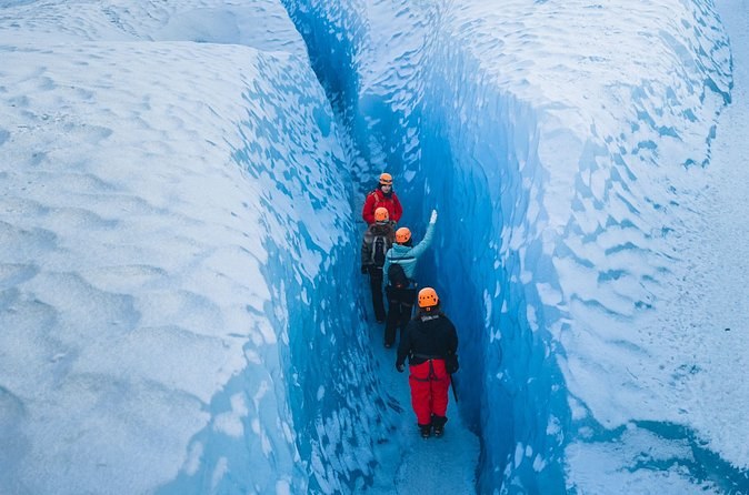 Four hikers in single file squeezing along the floor of a narrow blue crevasse