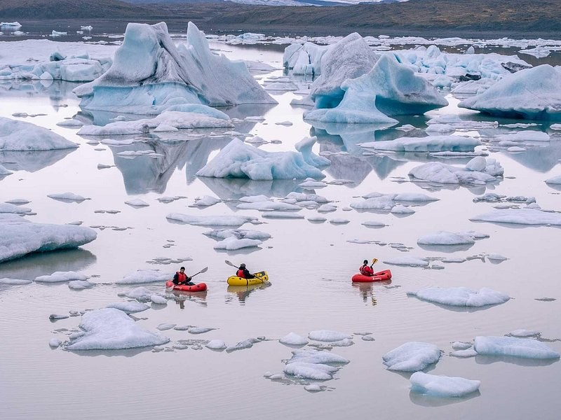 Three small inflatable boats paddling between icebergs on a pale lagoon, from above